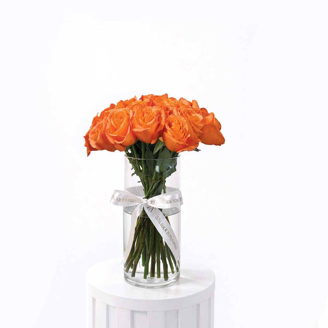 25 orange roses arranged in a clear glass vase on a white background