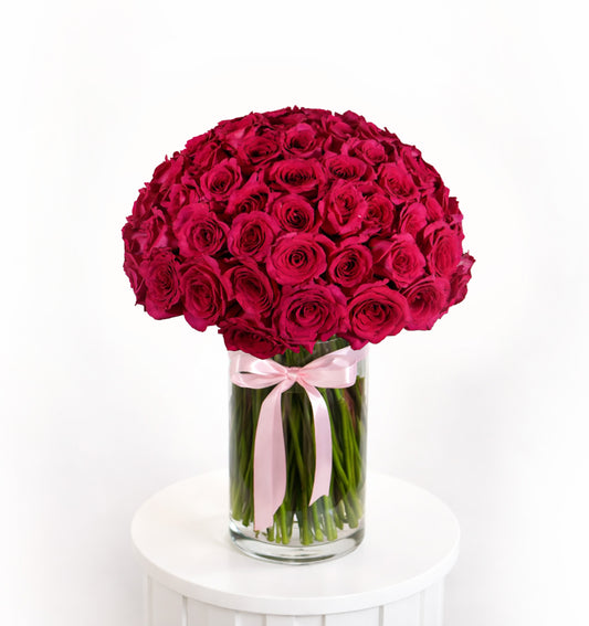 Massive dome arrangement of 100 vibrant fuchsia roses in a cylindrical glass vase with a signature Luxurious Flowers pink satin ribbon.