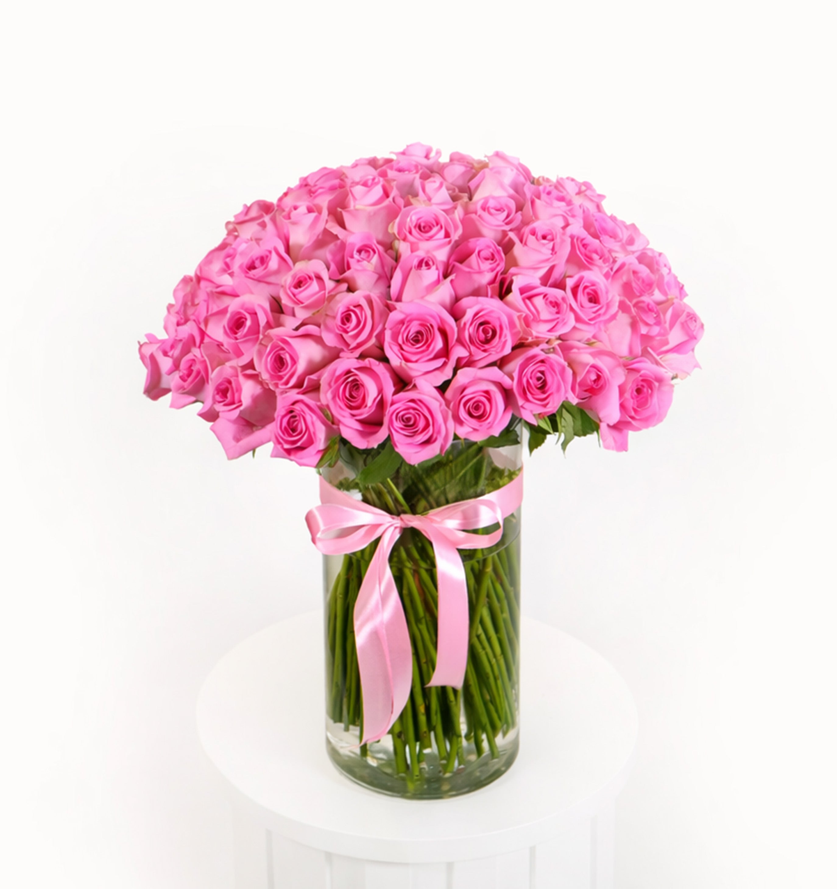 Grand arrangement of 100 vibrant pink roses in a cylindrical glass vase with a signature Luxurious Flowers pink satin ribbon