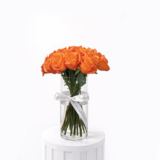 25 orange roses arranged in a clear glass vase on a white background