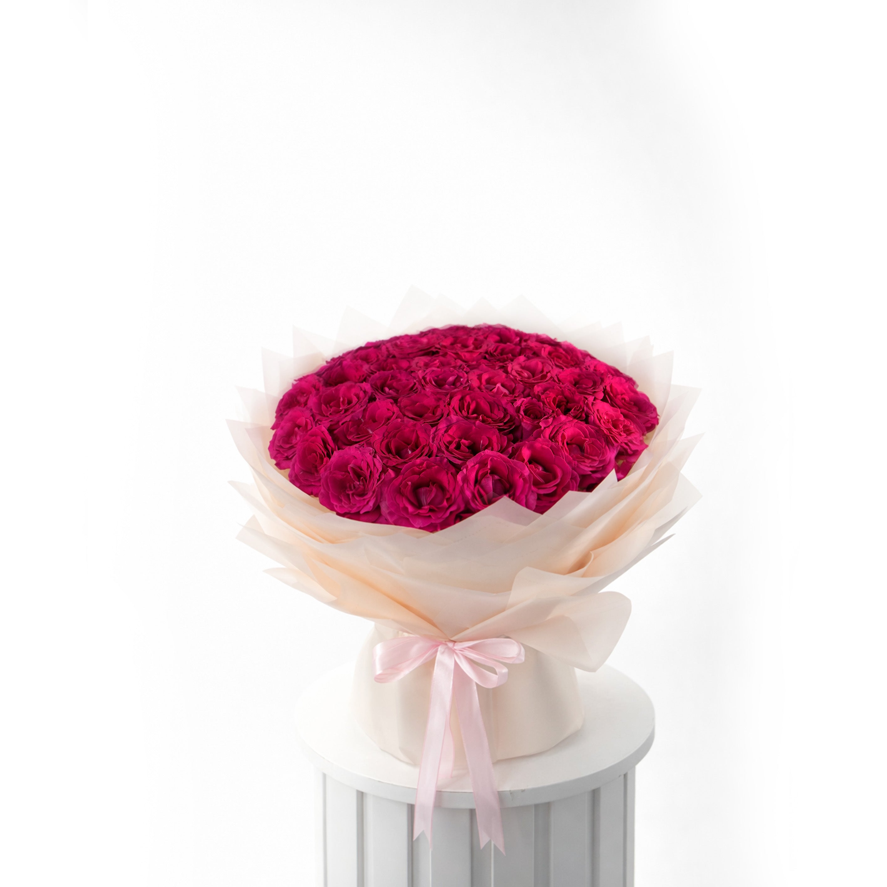 Bouquet of 50 magenta pink roses wrapped in cellophane with a pink ribbon on a white pedestal against a white background