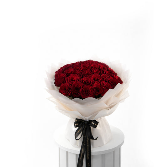 Bouquet of 50 red roses wrapped in white paper with a black ribbon on a white pedestal against a white background  for sale in Dubai 