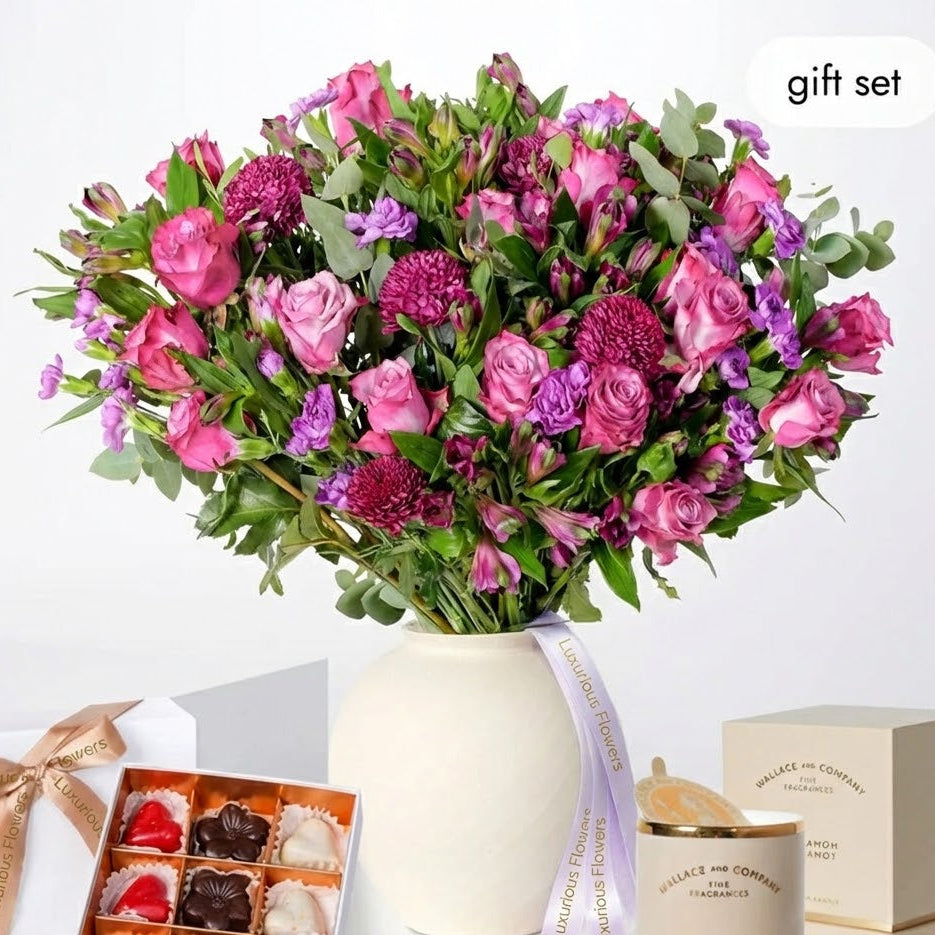 Bouquet of pink and purple flowers in a white vase with a box of chocolates and a candle on a white background for sale in Dubai
