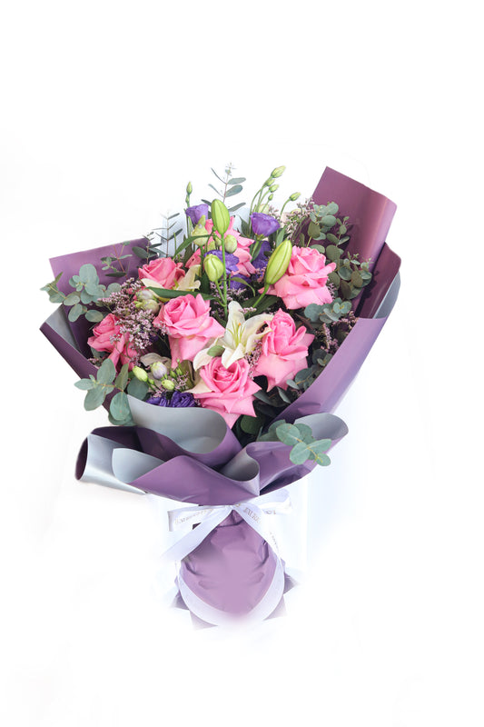 Bouquet of pink flowers with greenery wrapped in purple paper on a white background