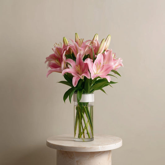 Bouquet of pink lilies in a clear vase on a marble pedestal against a beige background for sale in dubai