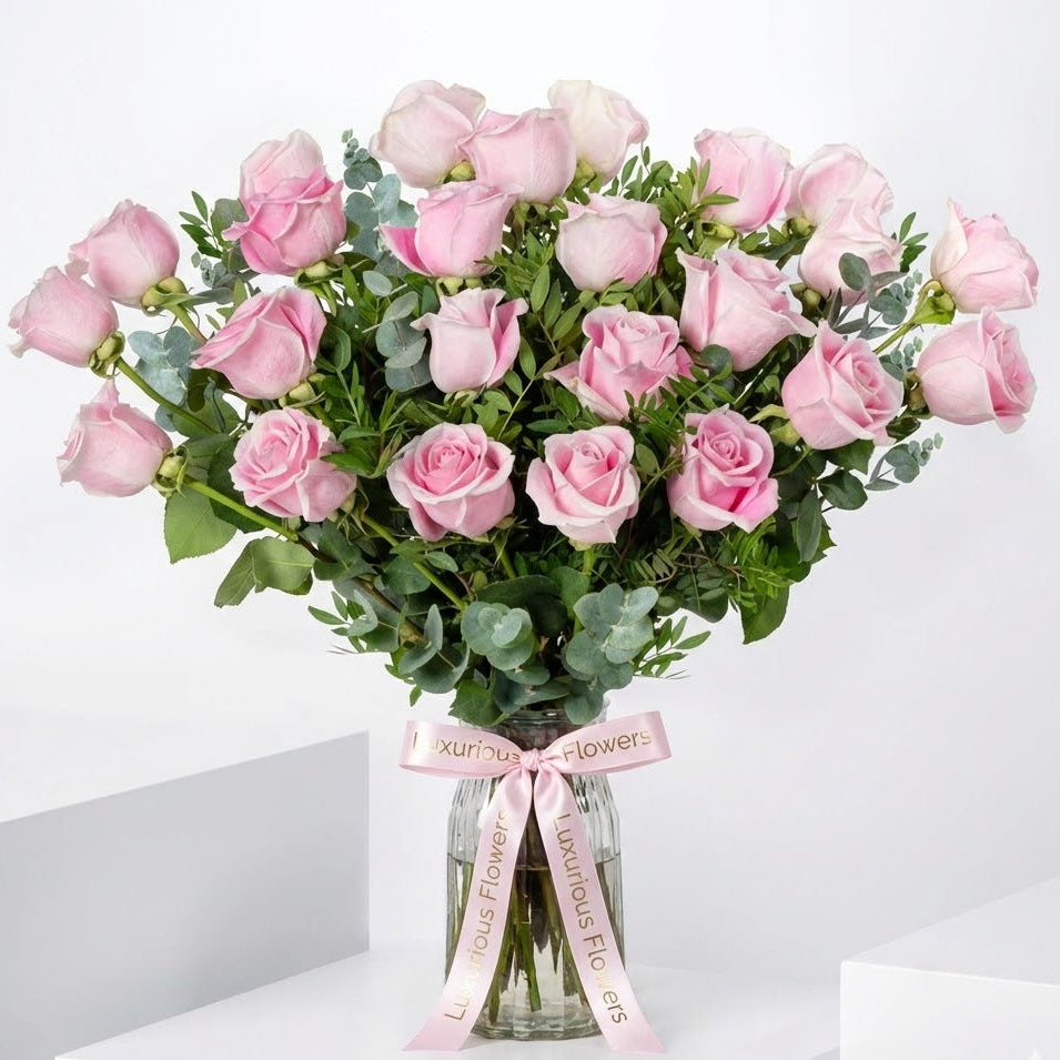 Bouquet of pink roses in a clear vase with a pink ribbon on a white background