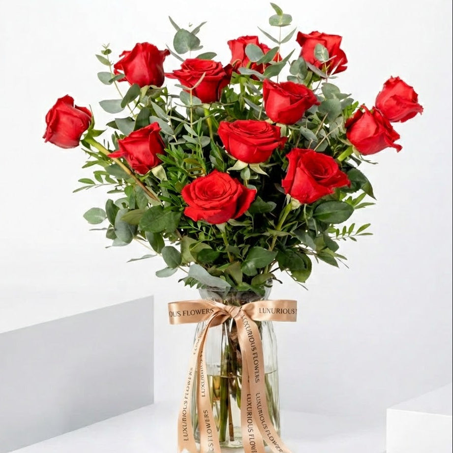 Bouquet of red roses in a clear vase with a ribbon on a white background