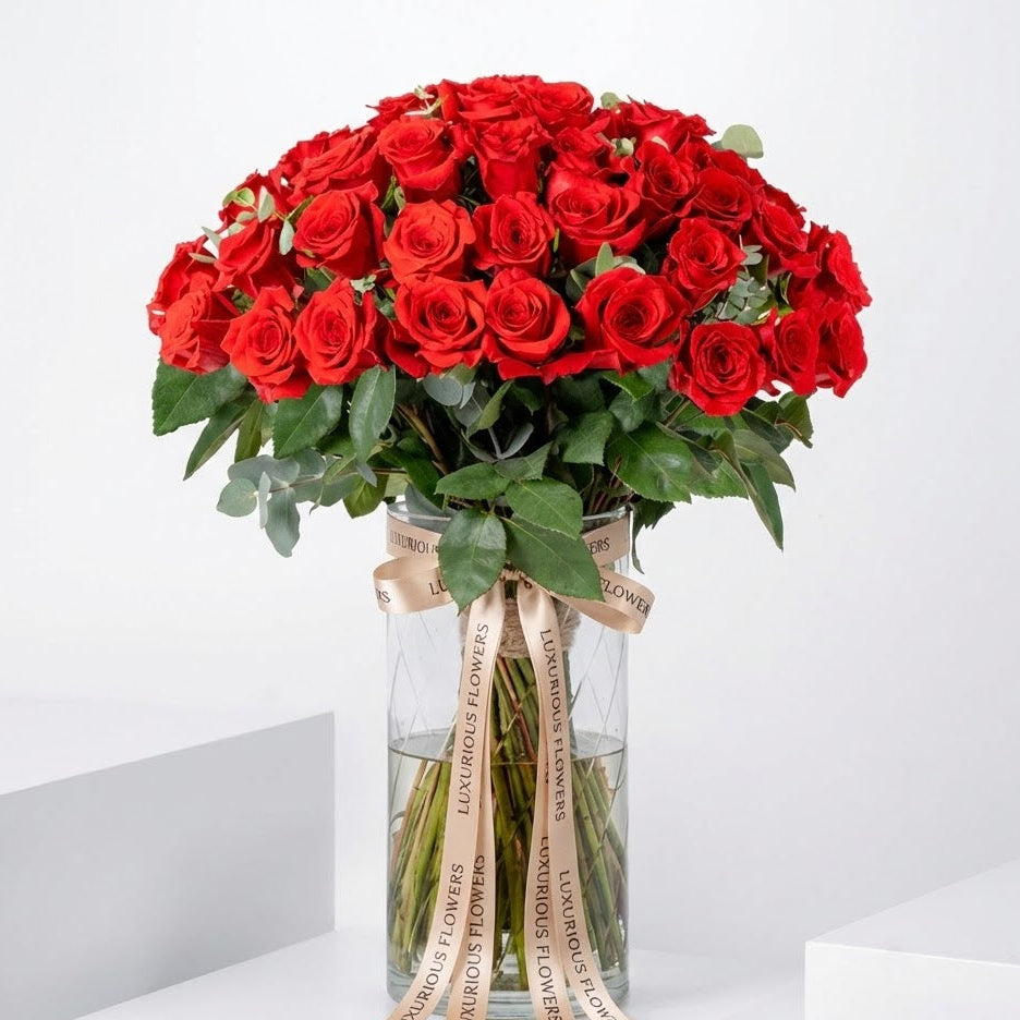 Bouquet of red roses in a clear vase with greenery on a white background