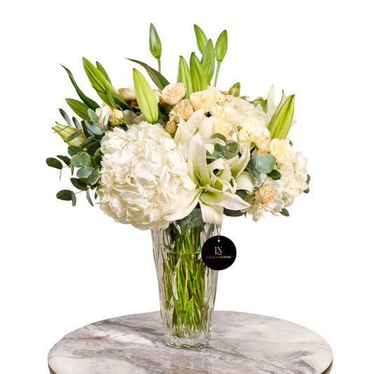 Bouquet of white and green flowers in a clear vase on a marble surface with a white background