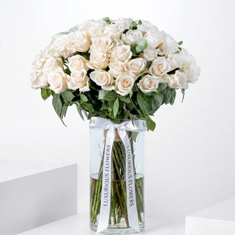 Bouquet of white roses in a clear vase with 'Luxurious Flowers' ribbon on a white background