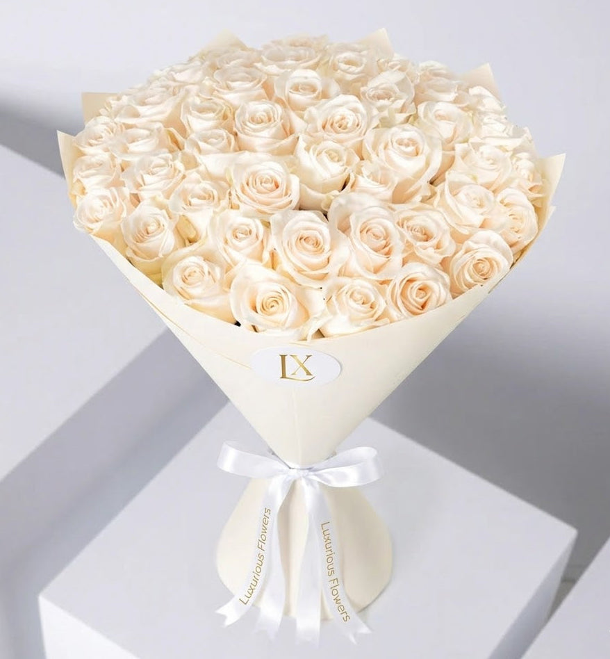 Bouquet of white roses in a cone-shaped paper holder with a white ribbon on a light gray background.