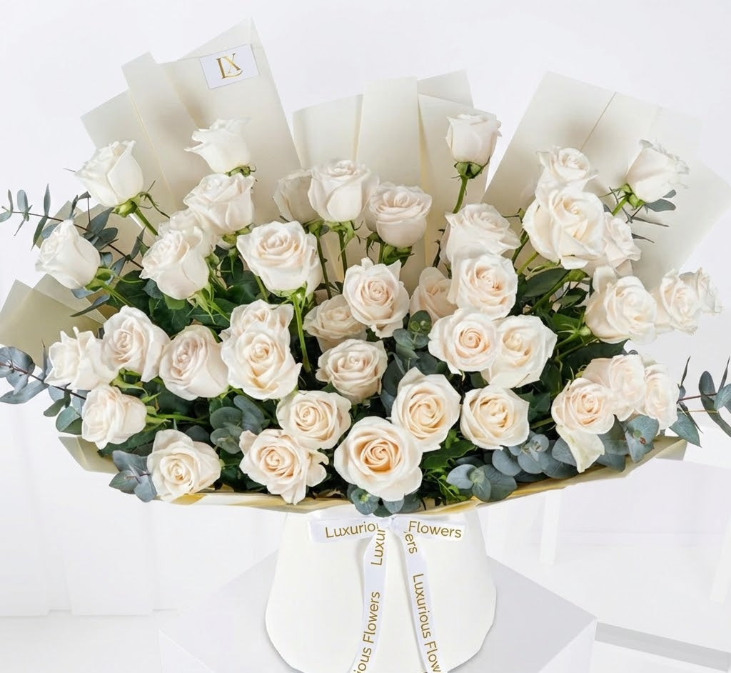 Bouquet of white roses with greenery in a box, branded 'Luxurious Flowers', on a white background.
