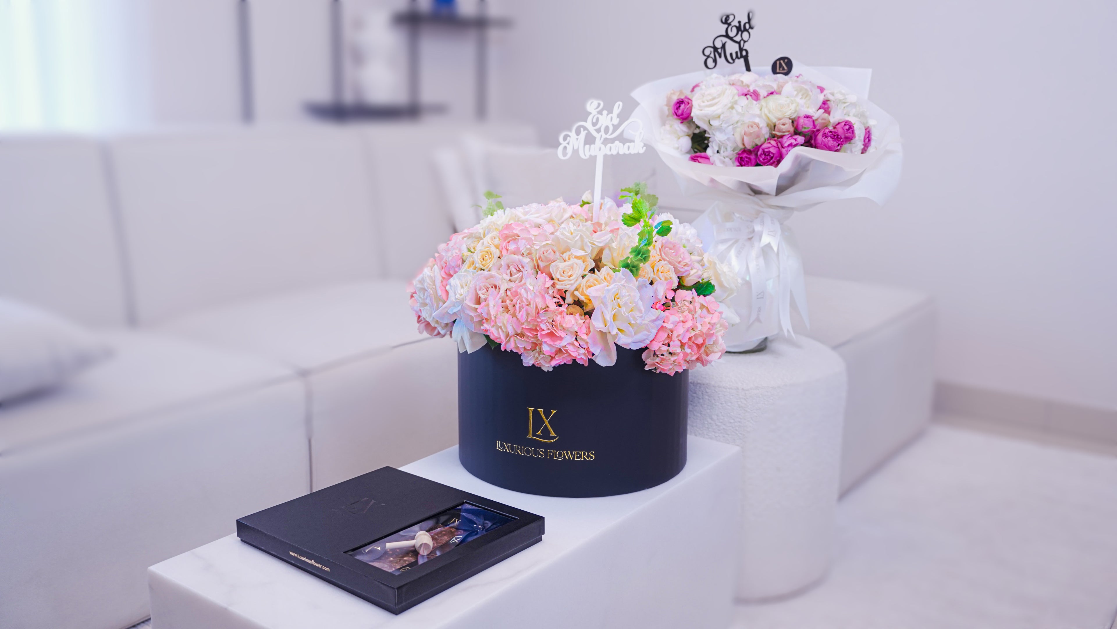 Decorative flower arrangement in a black box with a white sofa and decorative items in the background.