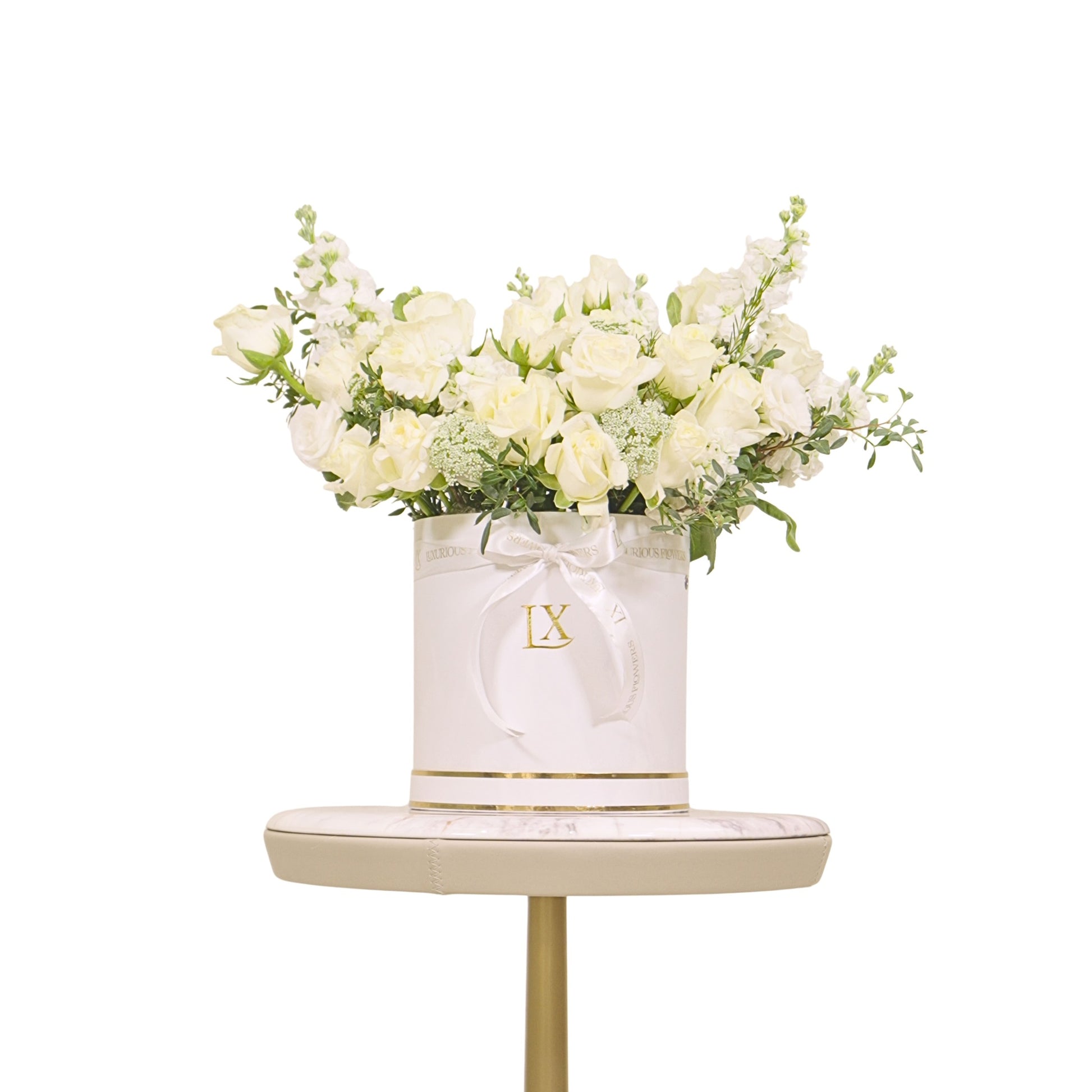 White flowers in a decorative box with 'LX' logo on a small table against a white background