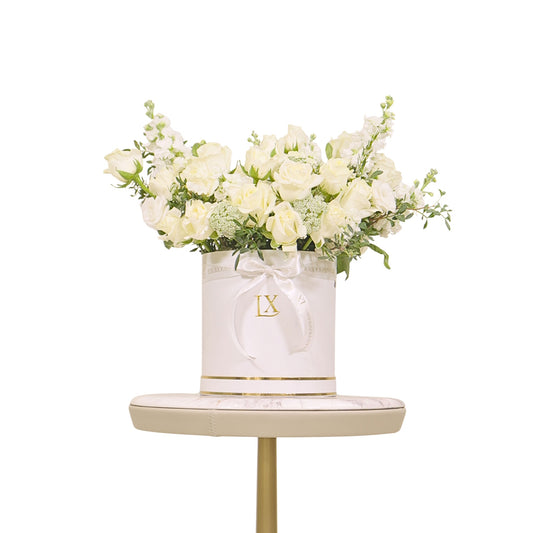 White flowers in a decorative box with 'LX' logo on a small table against a white background