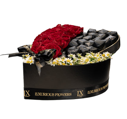 Heart-shaped flower box with red roses, black stones, and white flowers, branded 'Luxurious Flowers'.