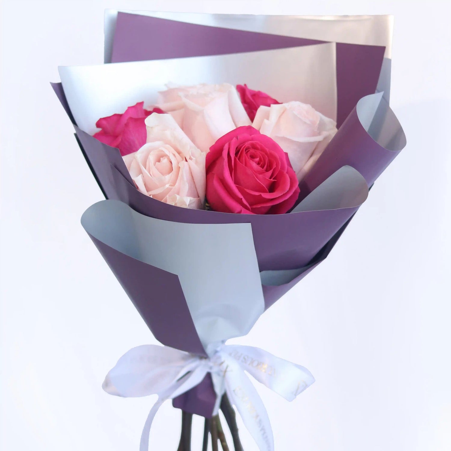 buy Bouquet of pink and red roses wrapped in purple paper with a white ribbon on a light gray background
