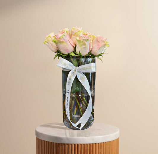 Clear vase with pink roses and a white ribbon on a beige background