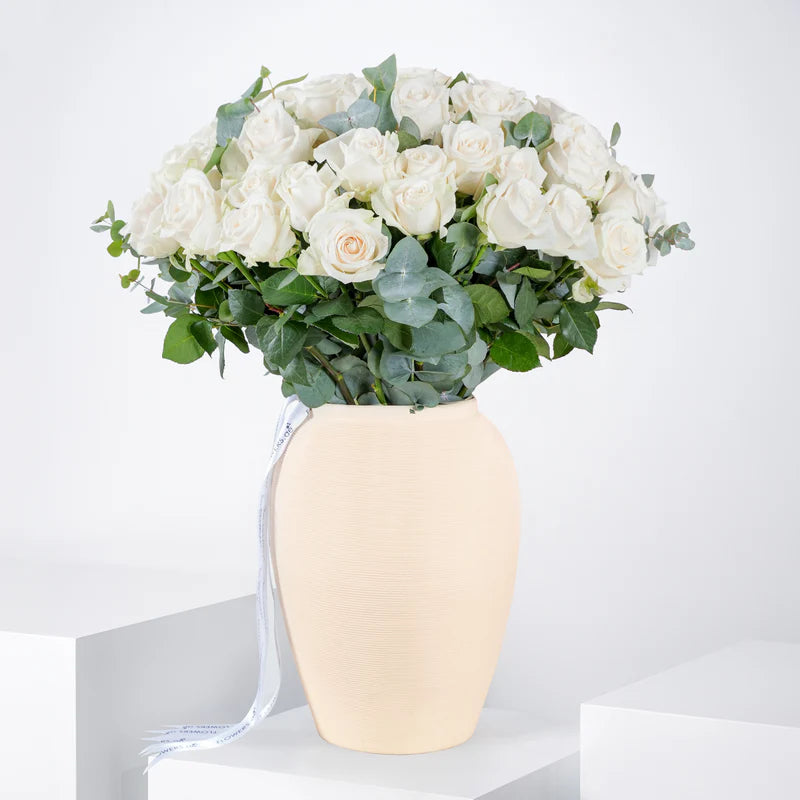 White flowers in a beige vase on a white surface with a light gray background