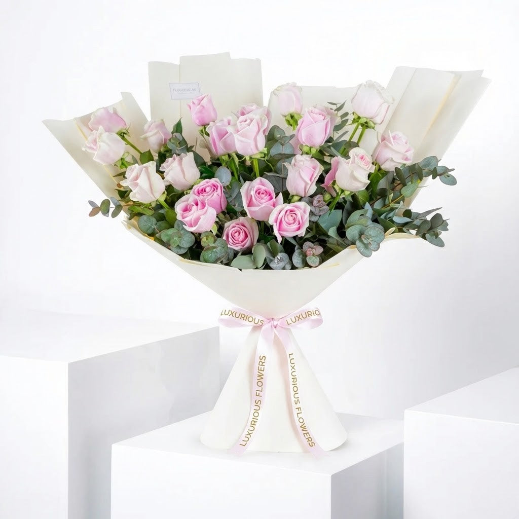A luxury hand-tied bouquet of ombre pink roses and eucalyptus sprigs wrapped in structured white pleated paper with a pink Luxurious Flowers ribbon.