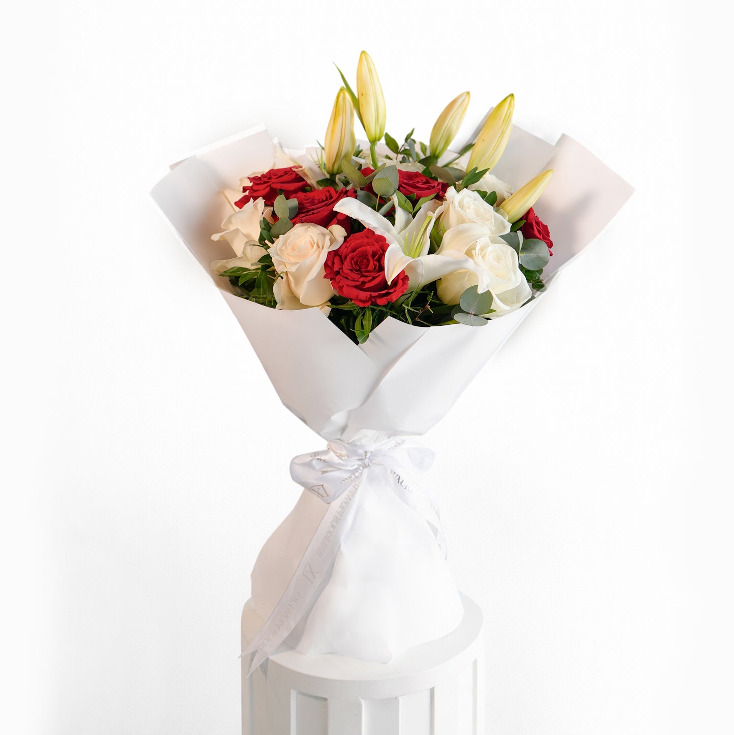 A luxury hand-tied bouquet featuring red roses, white roses, and white lilies in a cream pleated designer wrap with a Luxurious Flower ribbon.