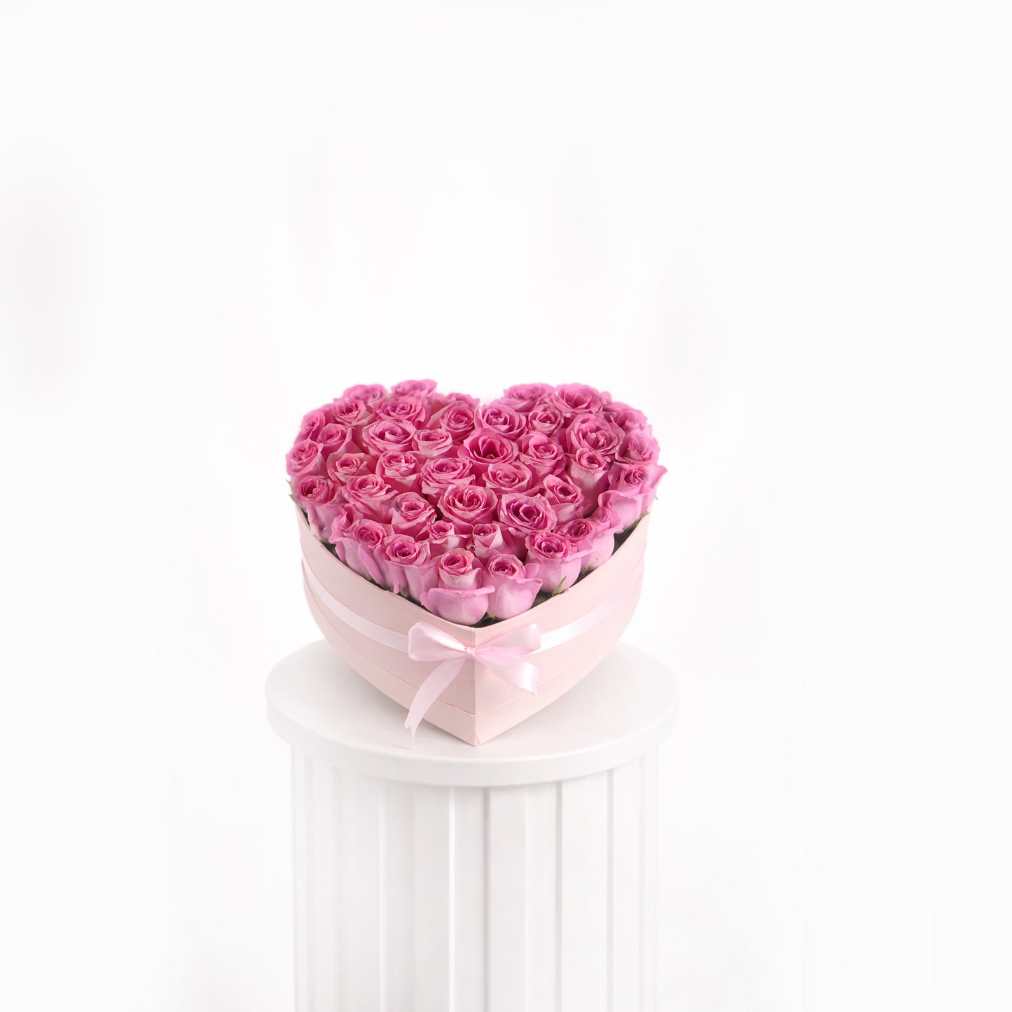 Heart-shaped bouquet of pink roses in heart a box on a white pedestal with a white background for sale in dubai